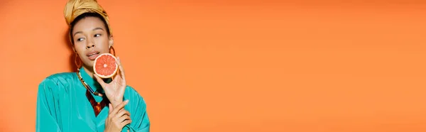 Well dressed african american woman holding fresh grapefruit on orange background, banner — Stock Photo