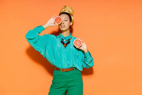 Modelo afroamericano de moda que cubre la cara con pomelo cortado sobre fondo naranja - foto de stock