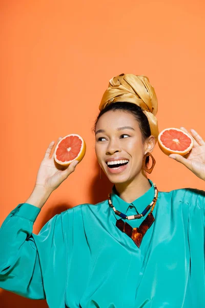 Positivo modello afroamericano in abiti luminosi con pompelmo organico su sfondo arancione — Foto stock