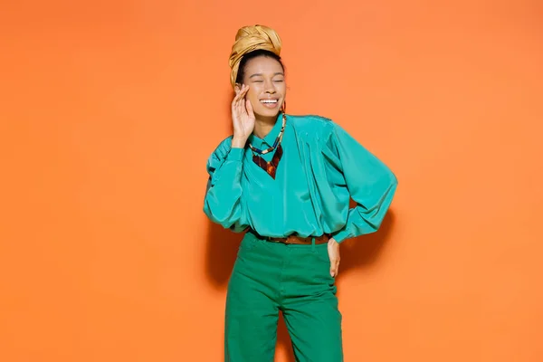 Sonriente modelo afroamericano en blusa brillante de pie sobre fondo naranja - foto de stock