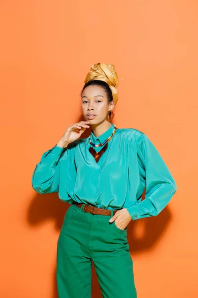 Modelo afroamericano de moda en traje brillante de pie sobre fondo naranja - foto de stock