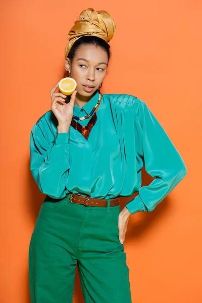 Mujer afroamericana de moda sosteniendo limón y posando sobre fondo naranja - foto de stock