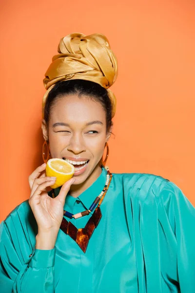 Портрет стильной африканской женщины, кусающей лимон на оранжевом фоне — стоковое фото