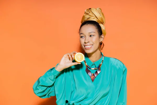Беззаботная африканская американская модель в летнем наряде держит лимон на оранжевом фоне — стоковое фото