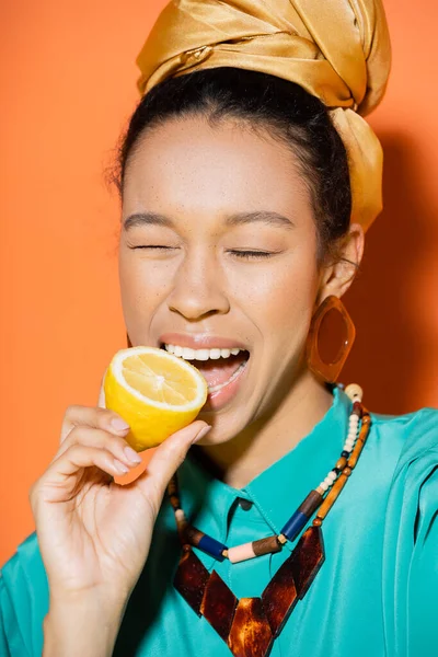 Trendy african american woman biting fresh lemon on orange background — Stock Photo