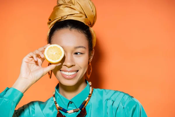 Mujer afroamericana de moda sonriendo y sosteniendo limón sobre fondo naranja - foto de stock