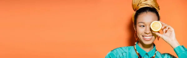 Modèle afro-américain tendance souriant et tenant du citron coupé sur fond orange, bannière — Photo de stock