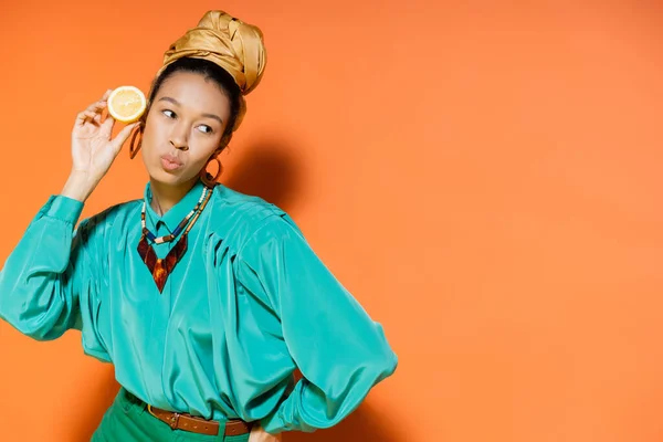 Stylish african american model pouting lips and holding cut lemon on orange background — Stock Photo