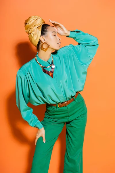 Vista lateral de la modelo afroamericana de moda posando en ropa de verano sobre fondo naranja - foto de stock