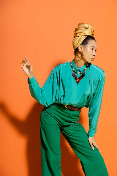 Fashionable african american model in bright clothes and headband on orange background — Stock Photo