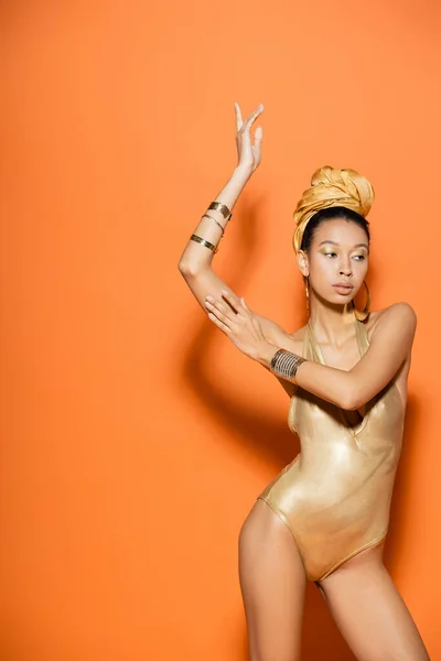 Modelo afroamericano de moda en pañuelo y traje de baño posando sobre fondo naranja - foto de stock