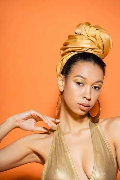 Portrait de joli modèle afro-américain en maillot de bain doré regardant la caméra sur fond orange — Photo de stock