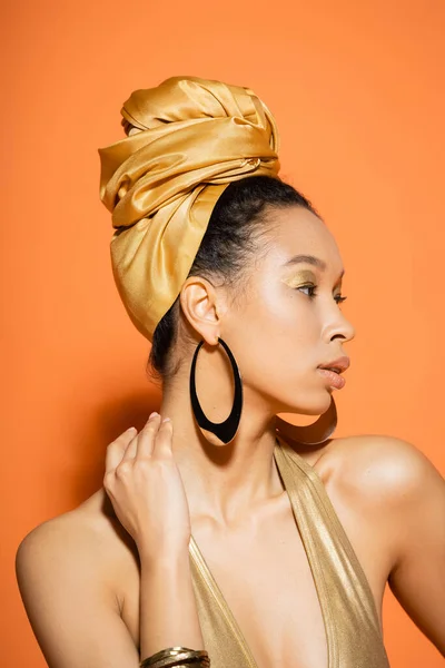 Porträt einer trendigen Afroamerikanerin mit goldenem Kopftuch auf orangefarbenem Hintergrund — Stockfoto
