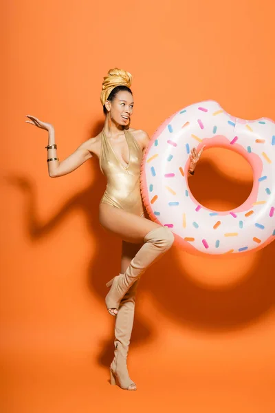 Alegre modelo afroamericano en traje de baño de moda celebración de anillo de piscina sobre fondo naranja - foto de stock