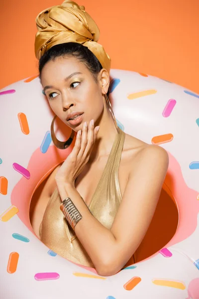 Портрет модной африканской модели в купальнике, держащей кольцо у бассейна на оранжевом фоне — стоковое фото