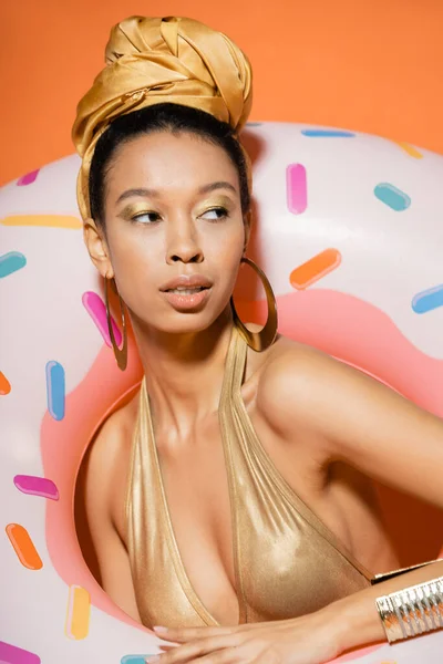 Portrait de modèle afro-américain à la mode en maillot de bain posant près de l'anneau de piscine sur orange — Photo de stock