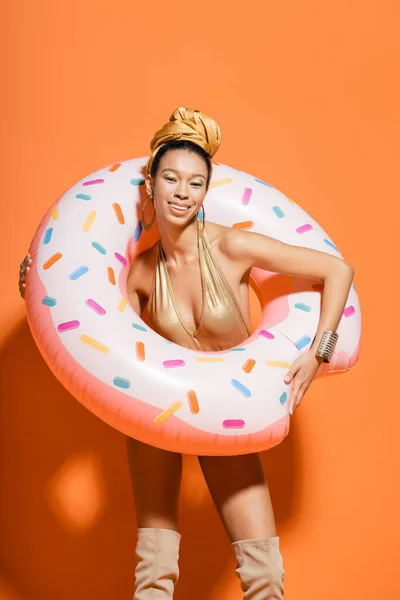 Mujer afroamericana muy alegre en traje de baño sosteniendo anillo de piscina sobre fondo naranja - foto de stock