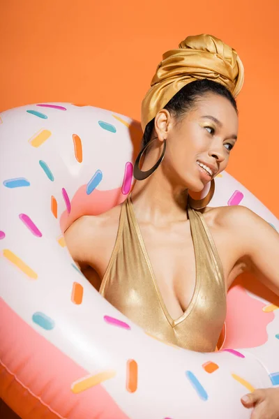 Portrait of fashionable african american woman smiling and holding pool ring on orange background — Stock Photo