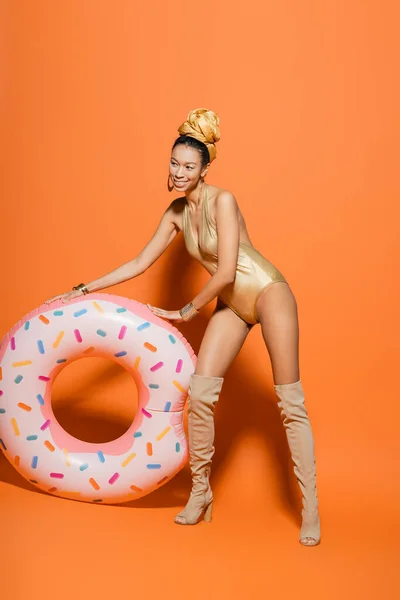 Unbekümmertes afrikanisch-amerikanisches Model in Badeanzug und Kopftuch posiert in der Nähe eines Pool-Rings auf orangefarbenem Hintergrund — Stockfoto