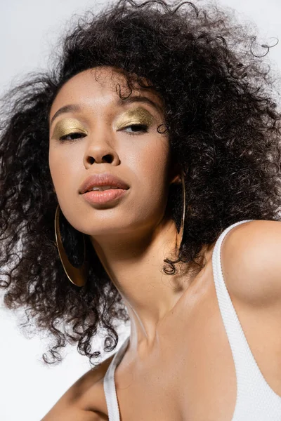 Portrait of curly african american woman with golden eye shadows looking away isolated on grey — Stock Photo