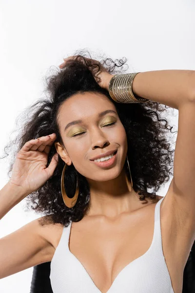 African american model with closed eyes adjusting curly hair isolated on white — Stock Photo