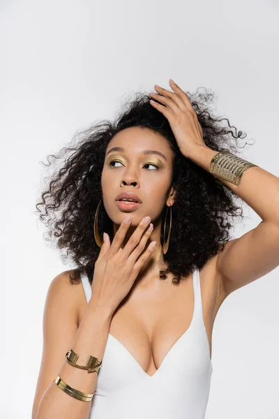 Giovane modello afroamericano che regola i capelli ricci e distoglie lo sguardo isolato sul grigio — Foto stock