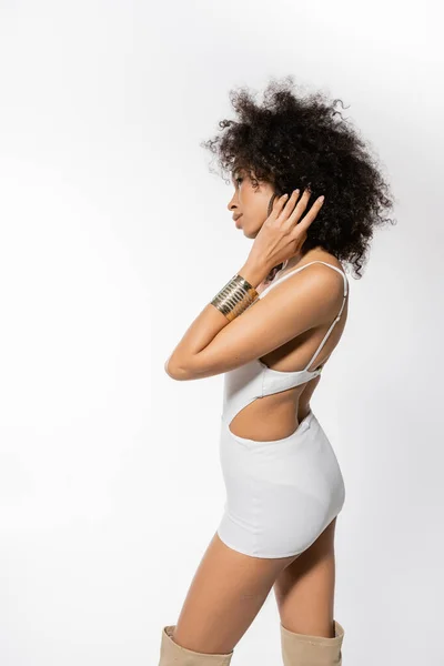 Vista laterale della giovane modella afroamericana con i capelli ricci in posa in mini abito bianco su sfondo grigio — Foto stock