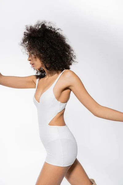 Side view of young african american model with curly hair posing in tight mini dress on grey — Stock Photo