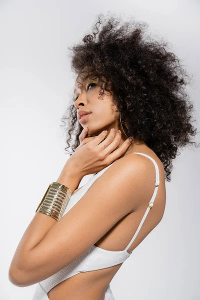 Bonita mujer afroamericana con brazalete de oro posando aislado en gris - foto de stock
