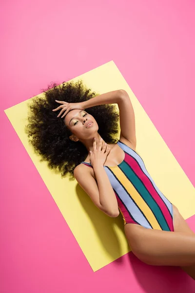 Top view of curly african american woman in colorful striped swimsuit posing on yellow and pink background — Stock Photo