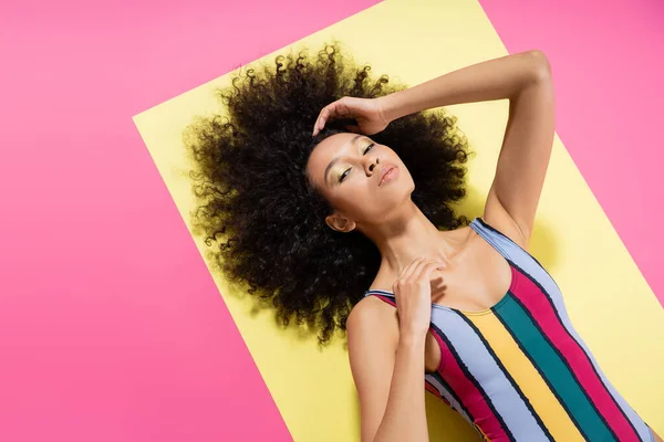 Top view of curly african american woman in colorful swimsuit lying on yellow and pink background — Stock Photo