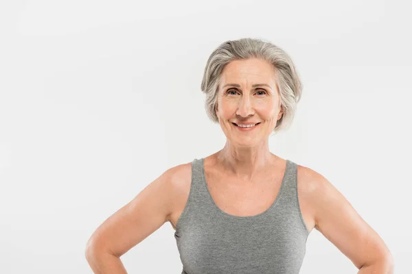 Athletic and senior woman in tank top smiling isolated on grey — Stock Photo
