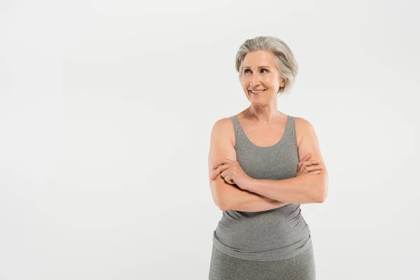 Donna allegra e anziana in abbigliamento sportivo in piedi con braccia incrociate isolate su grigio — Foto stock