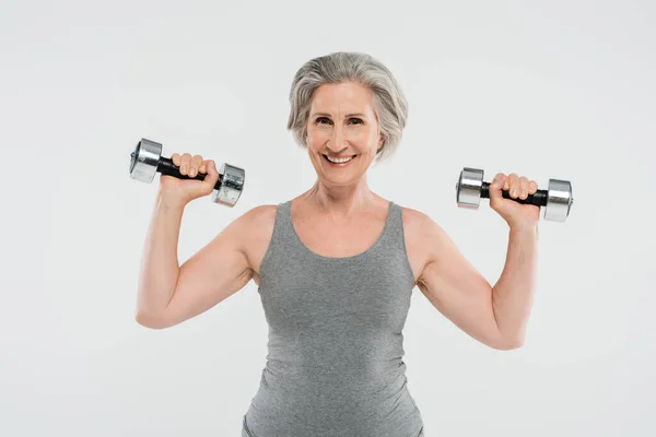 Excitada mulher idosa com cabelos grisalhos exercitando com halteres isolados em cinza — Fotografia de Stock
