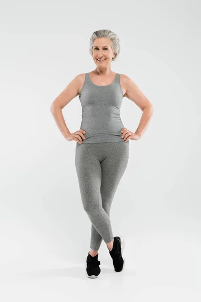 Full length of cheerful and retired woman in sportswear posing on grey — Stock Photo