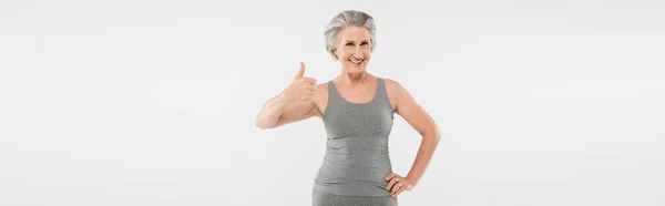 Mulher alegre e aposentado em sportswear posando com a mão no quadril e mostrando como isolado em cinza, banner — Fotografia de Stock