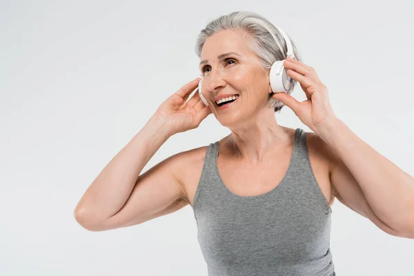 Feliz mujer mayor escuchando música en auriculares inalámbricos aislados en gris - foto de stock