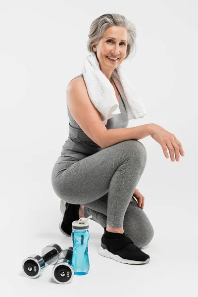 Full length of happy senior woman with towel on shoulder smiling while sitting on grey — Stock Photo