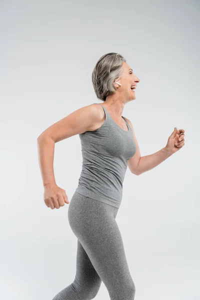 Seitenansicht einer fröhlichen Seniorin mit grauen Haaren, die vereinzelt auf grau läuft — Stockfoto