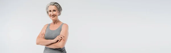 Carefree senior woman in sportswear standing with folded arms isolated on grey, banner — Stock Photo