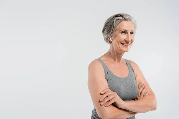 Positive Seniorin in Sportkleidung steht mit verschränkten Armen isoliert auf grau — Stockfoto