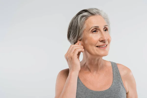 Happy senior woman adjusting wireless earphone isolated on grey — Stock Photo
