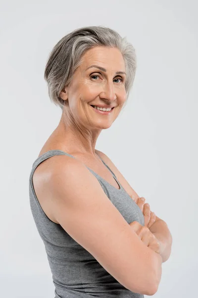 Felice donna anziana con i capelli grigi in piedi con le braccia incrociate isolato su grigio — Foto stock
