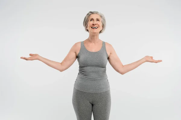 Satisfied senior woman with grey hair looking up and gesturing isolated on grey — Stock Photo