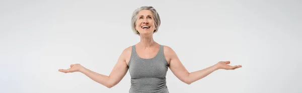Satisfied senior woman with grey hair looking up and gesturing isolated on grey, banner — Stock Photo