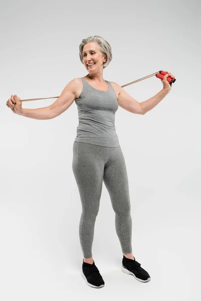 Full length of cheerful senior woman holding skipping rope on grey — Stock Photo