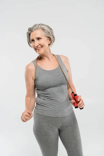 Zufriedene Seniorin mit grauen Haaren hält Springseil isoliert auf grau — Stockfoto