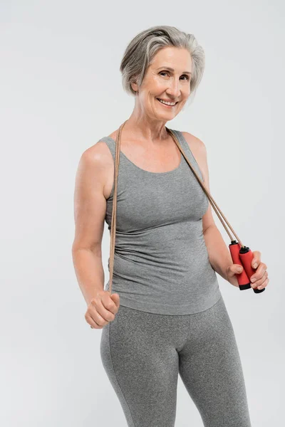 Donna anziana spensierata con capelli grigi che tiene la corda per saltare isolata su grigio — Foto stock