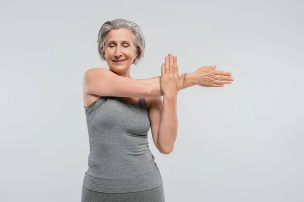 Cheerful grandmother with closed eyes working out and smiling isolated on grey — Stock Photo
