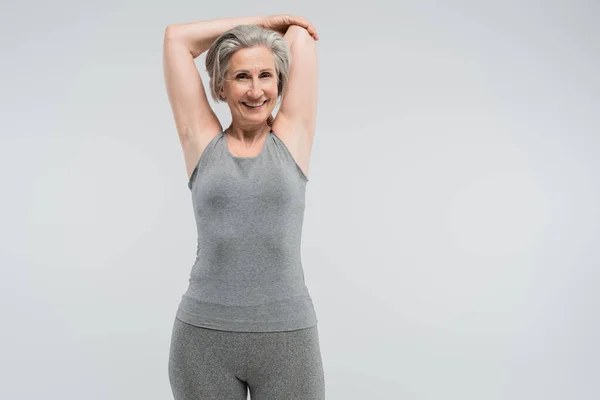 Радісна бабуся в спортивному одязі, що працює і посміхається ізольовано на сірому — стокове фото